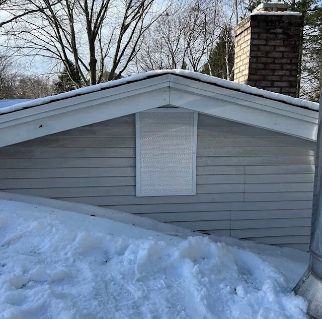 Gray aluminum soffit with exclusion screen vent installed on gable end, brick chimney visible
