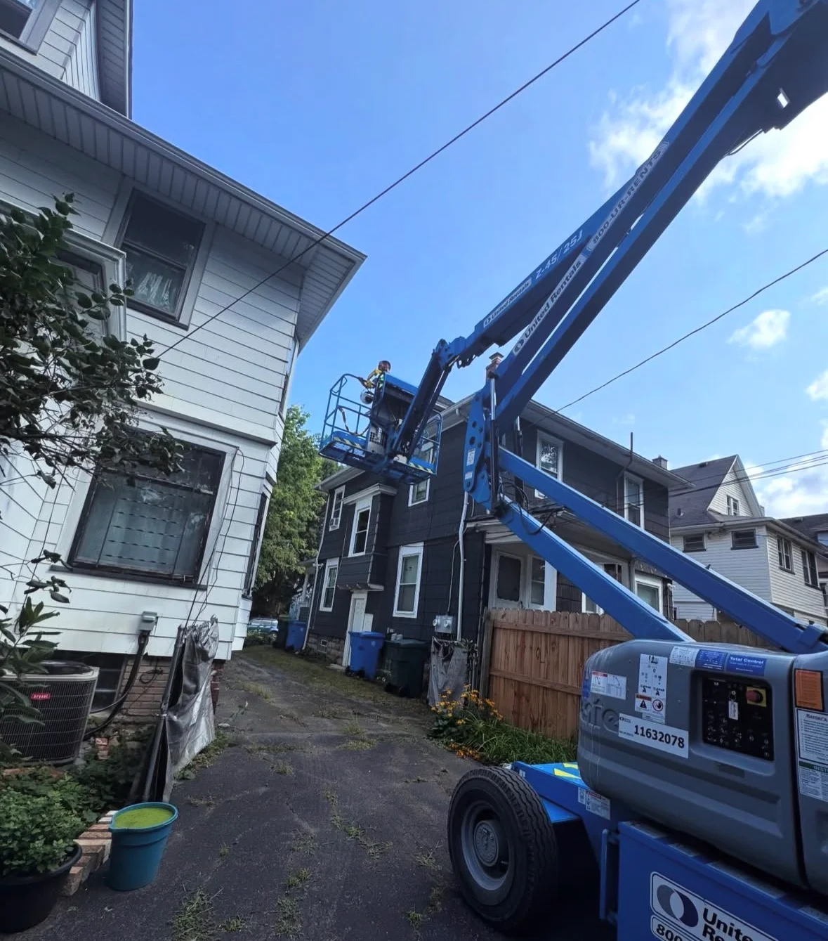 Blue articulating lift positioned at residential home for wildlife control access to upper floors and roof