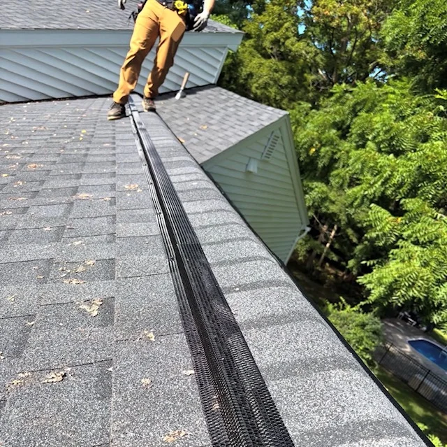 Worker installing black mesh gutter guard on asphalt shingle roof with cleaned gutters