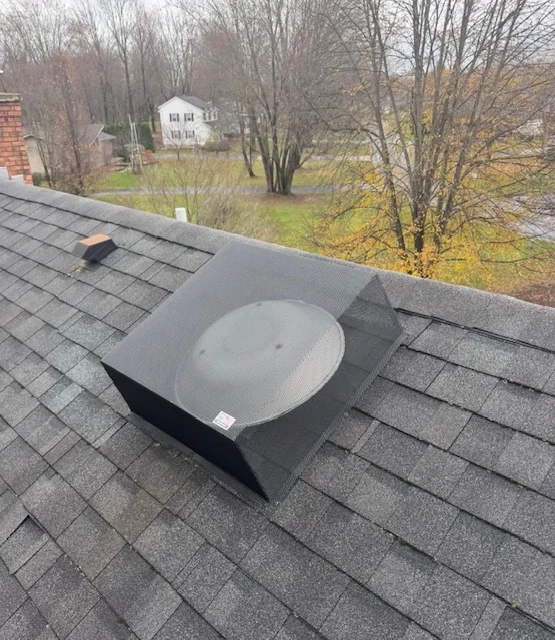 Metal roof vent exclusion cover installed on asphalt shingle roof with white dome vent and black metal frame